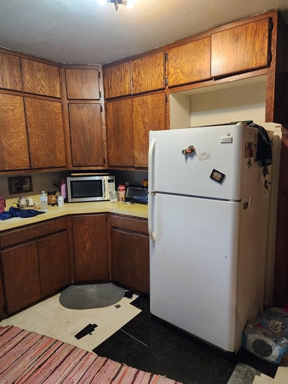 310 Mcgee St, Eufaula, OK 74432 - kitchen featuring freestanding refrigerator, stainless steel microwave, light countertops, and brown cabinets