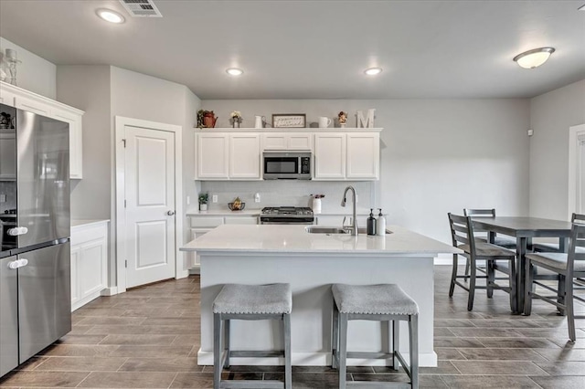 13091 Mannington Rd, Edmond, OK 73025 - kitchen with appliances with stainless steel finishes, wood tiled floors, a sink, white cabinets, and a kitchen bar