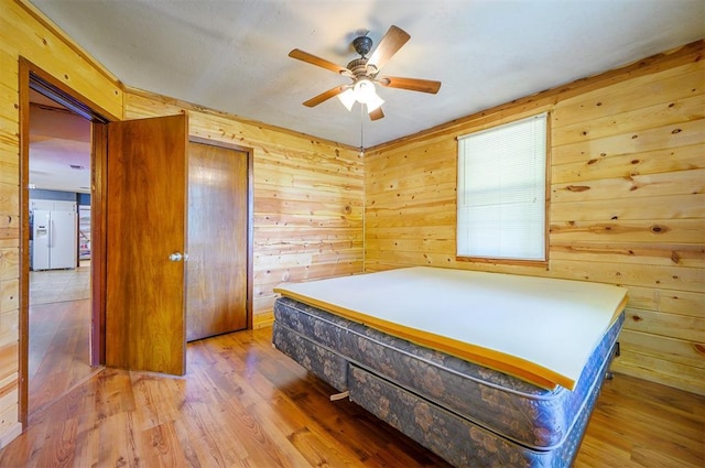 431 Canoe Rd, Broken Bow, OK 74728 - bedroom featuring white fridge with ice dispenser, wood finished floors, wooden walls, and a ceiling fan