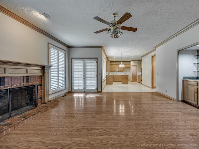 3713 Barwick Ct, Norman, OK 73072 - unfurnished living room with crown molding, a textured ceiling, light wood-style flooring, a ceiling fan, and a fireplace