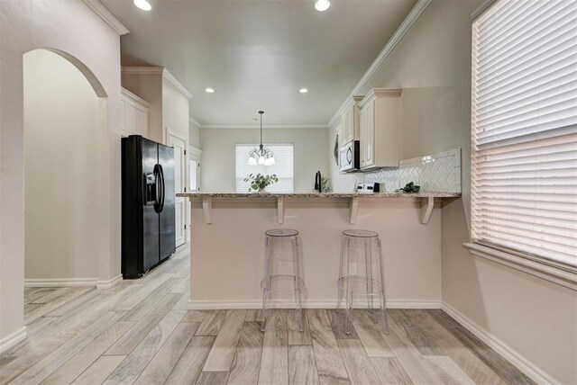 8340 NW 137th St, Oklahoma City, OK 73142 - kitchen featuring black fridge with ice dispenser, light stone counters, light wood-style flooring, white cabinetry, and recessed lighting