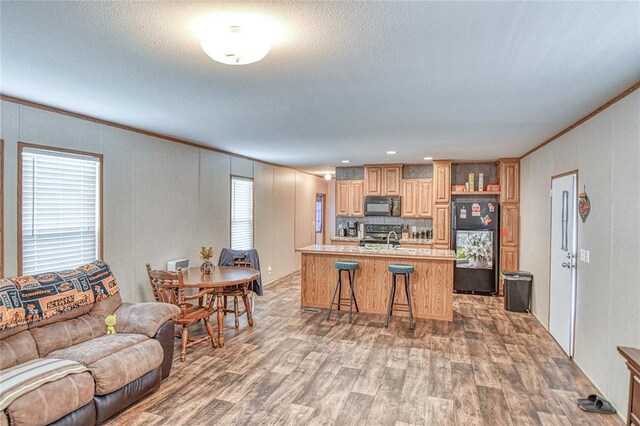 13086 240th, Blanchard, OK 73010 - kitchen with black appliances, light wood-style floors, crown molding, a kitchen island with sink, and a decorative wall