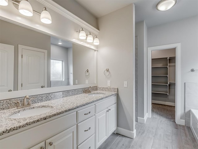 3713 Andrew Ct, Norman, OK 73072 - bathroom featuring double vanity, wood finished floors, a bath, a spacious closet, and baseboards