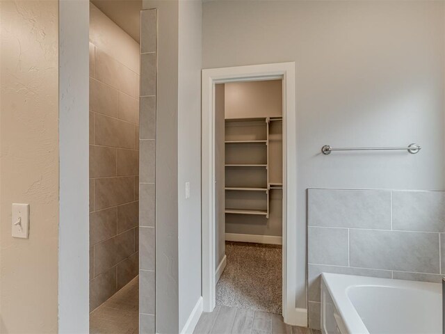 3713 Andrew Ct, Norman, OK 73072 - bathroom featuring a walk in closet, a garden tub, walk in shower, baseboards, and wood finished floors