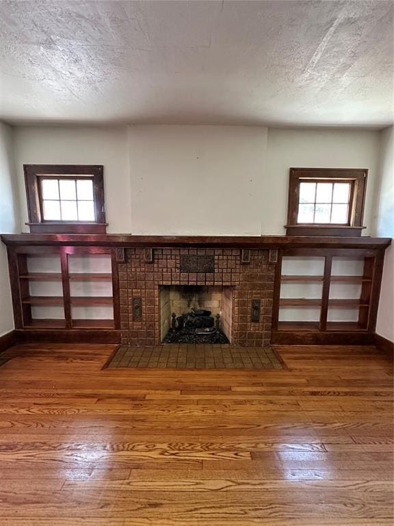 2001 NW 18th St, Oklahoma City, OK 73106 - unfurnished living room with a brick fireplace, wood-type flooring, plenty of natural light, and a textured ceiling