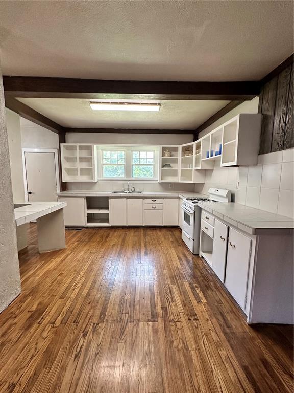 2001 NW 18th St, Oklahoma City, OK 73106 - kitchen featuring white gas range oven, beamed ceiling, open shelves, dark wood-style floors, and white cabinetry