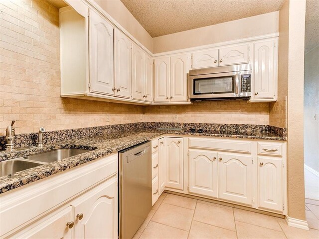 7817 Old Hickory Ln, Oklahoma City, OK 73116 - kitchen featuring stainless steel appliances, light tile patterned floors, dark stone countertops, and a textured ceiling