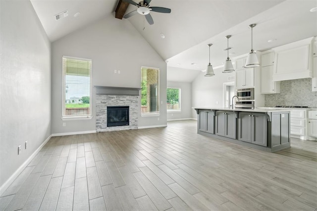 1513 Reid Pryor Rd, Norman, OK 73072 - unfurnished living room featuring ceiling fan, beam ceiling, high vaulted ceiling, light wood finished floors, and a glass covered fireplace