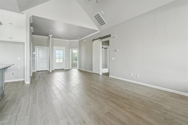 1513 Reid Pryor Rd, Norman, OK 73072 - unfurnished living room with a barn door, crown molding, light wood-style flooring, and lofted ceiling