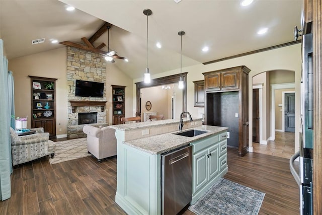 kitchen with dishwasher, open floor plan, a sink, a stone fireplace, and a ceiling fan