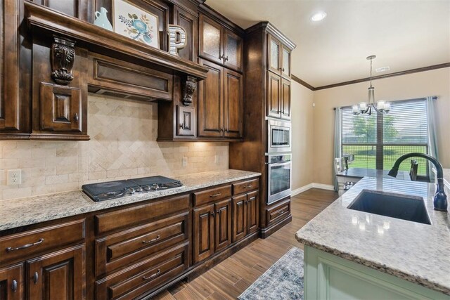 kitchen with appliances with stainless steel finishes, a sink, a chandelier, tasteful backsplash, and crown molding