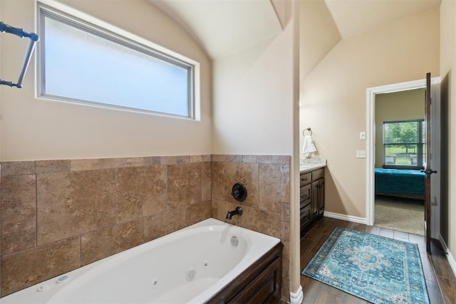 full bath with a jetted tub, lofted ceiling, vanity, and wood finished floors