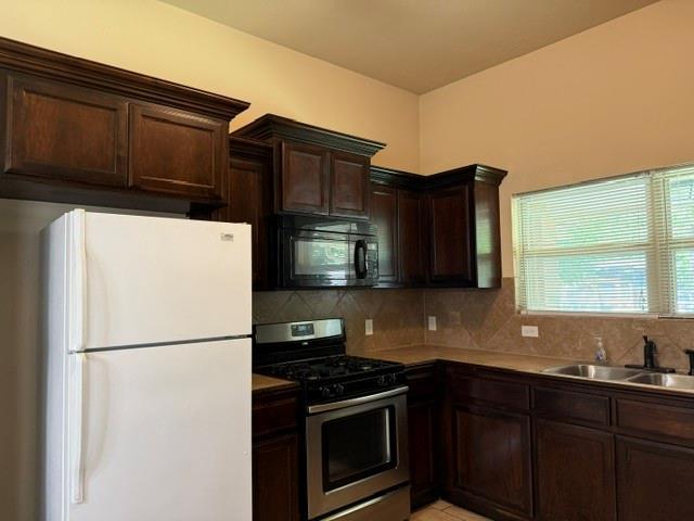1523 Morland St, Norman, OK 73071 - kitchen with freestanding refrigerator, stainless steel gas range, black microwave, a sink, and dark brown cabinets