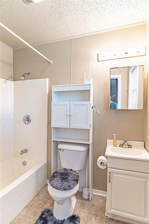 1343 E Moses St, Cushing, OK 74023 - bathroom featuring vanity, a textured ceiling, bathtub / shower combination, tile patterned flooring, and toilet