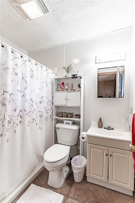 1343 E Moses St, Cushing, OK 74023 - bathroom with toilet, vanity, a textured ceiling, tile patterned flooring, and a shower with curtain