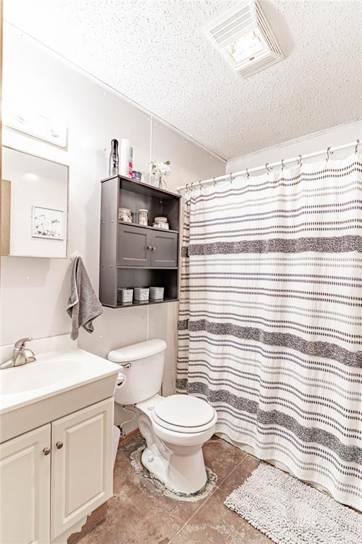 1343 E Moses St, Cushing, OK 74023 - bathroom featuring a textured ceiling, toilet, vanity, tile patterned floors, and a shower with curtain