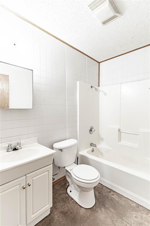 1343 E Moses St, Cushing, OK 74023 - full bathroom with toilet, tile walls, vanity, bathtub / shower combination, and a textured ceiling