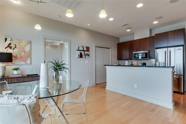 301 NE 4th St Unit 10, Oklahoma City, OK 73104 - kitchen with appliances with stainless steel finishes, dark countertops, light wood-style flooring, backsplash, and hanging light fixtures
