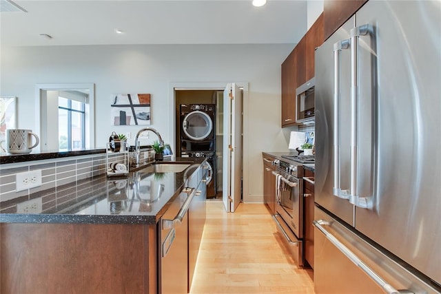 301 NE 4th St Unit 10, Oklahoma City, OK 73104 - kitchen featuring stainless steel appliances, stacked washing machine and dryer, a sink, light wood finished floors, and dark stone counters