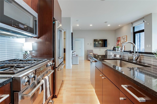 301 NE 4th St Unit 10, Oklahoma City, OK 73104 - kitchen with appliances with stainless steel finishes, a sink, light wood-style flooring, backsplash, and dark stone counters