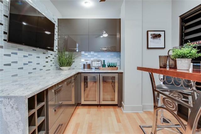 301 NE 4th St Unit 10, Oklahoma City, OK 73104 - kitchen featuring wine cooler, light stone countertops, backsplash, light wood-style floors, and gray cabinetry