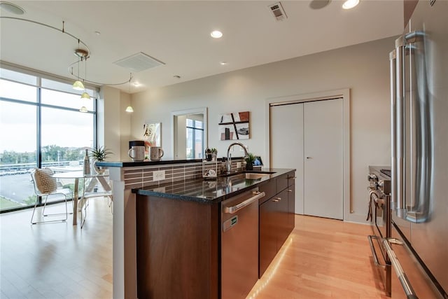 301 NE 4th St Unit 10, Oklahoma City, OK 73104 - kitchen featuring high quality appliances, a sink, light wood-style floors, dark stone countertops, and a kitchen island with sink