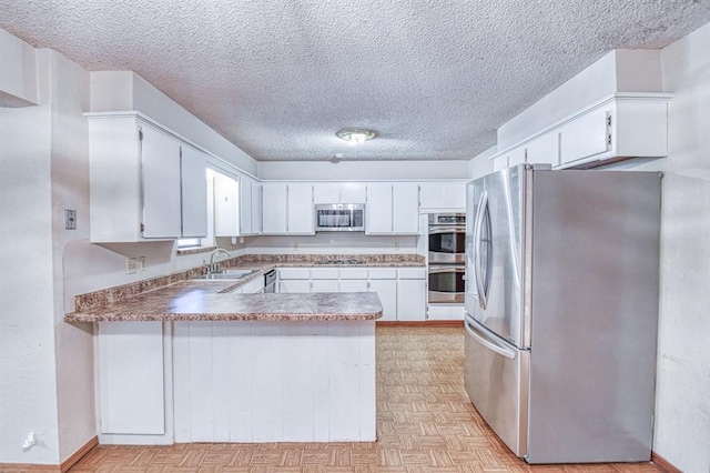 2804 Meadow Ave, Norman, OK 73072 - kitchen featuring appliances with stainless steel finishes, a peninsula, a textured ceiling, a sink, and white cabinetry