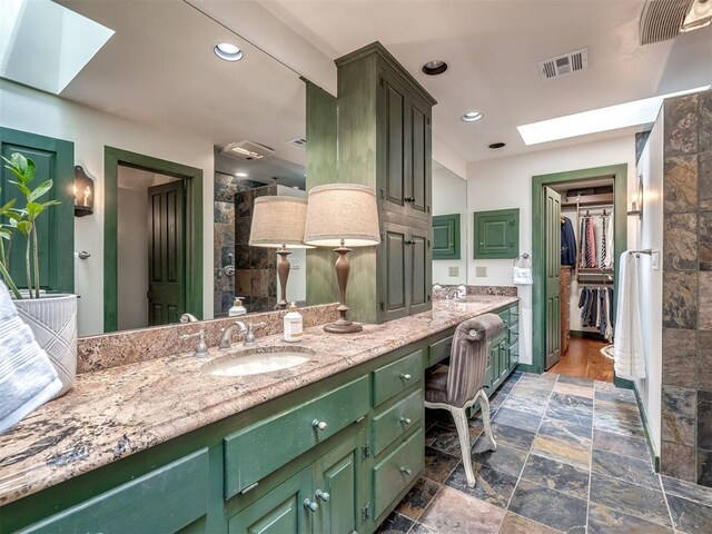 4005 NE 122nd St, Edmond, OK 73013 - bathroom featuring a skylight, double vanity, stone finish flooring, recessed lighting, and a tile shower