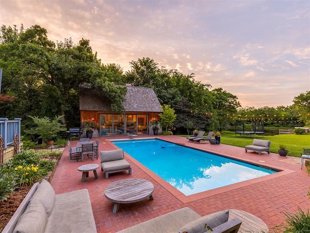 4005 NE 122nd St, Edmond, OK 73013 - pool at dusk featuring an exterior structure, a trampoline, a patio area, a yard, and an outbuilding