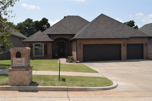 1713 Rain Tree Ln, Midwest City, OK 73130 - french country home with an attached garage, brick siding, driveway, a front lawn, and roof with shingles