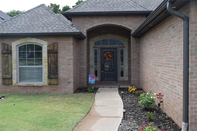 1713 Rain Tree Ln, Midwest City, OK 73130 - view of exterior entry featuring roof with shingles, brick siding, and a yard