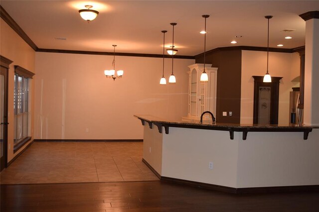 1713 Rain Tree Ln, Midwest City, OK 73130 - kitchen featuring a kitchen breakfast bar, ornamental molding, hanging light fixtures, wood finished floors, and dark stone countertops