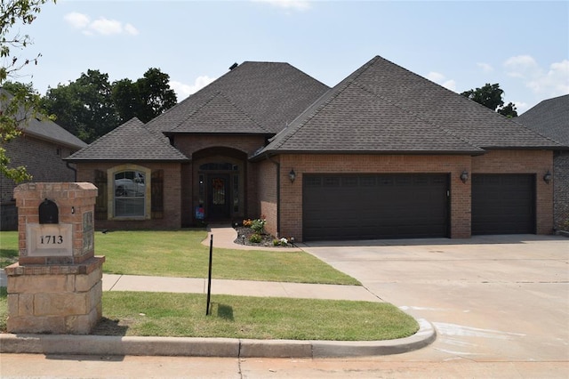 1713 Rain Tree Ln, Midwest City, OK 73130 - french country inspired facade featuring an attached garage, brick siding, a shingled roof, and concrete driveway