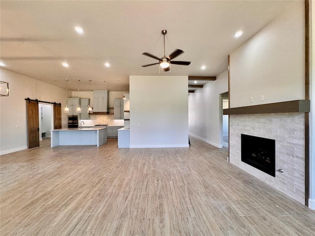 10165 NW 100th St, Yukon, OK 73099 - unfurnished living room featuring a barn door, ceiling fan, light wood finished floors, a fireplace, and recessed lighting
