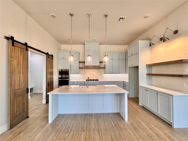10165 NW 100th St, Yukon, OK 73099 - kitchen featuring appliances with stainless steel finishes, a barn door, light wood-style floors, and backsplash