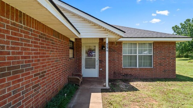 677 S Morgan Ave, Blanchard, OK 73010 - view of exterior entry with brick siding, roof with shingles, and a lawn