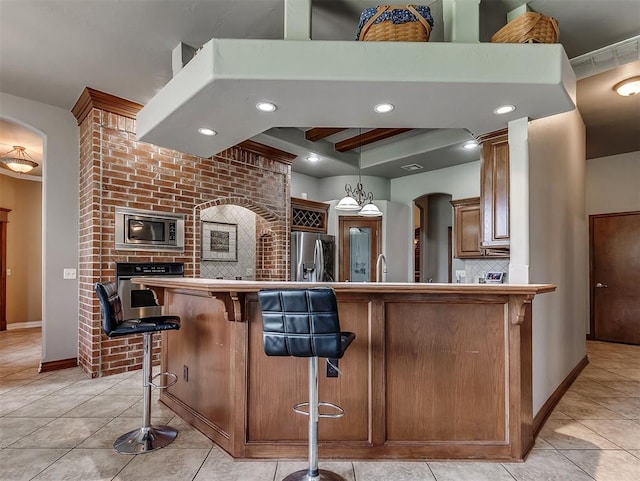1316 NW 171st St, Edmond, OK 73012 - kitchen featuring appliances with stainless steel finishes, light tile patterned floors, arched walkways, and a breakfast bar area