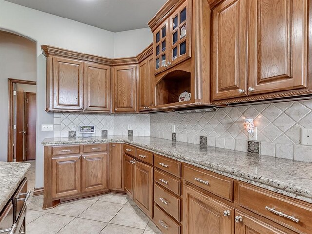 1316 NW 171st St, Edmond, OK 73012 - kitchen with arched walkways, light stone counters, light tile patterned floors, and brown cabinetry