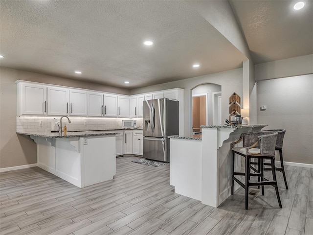 6513 NW 95th St, Oklahoma City, OK 73162 - kitchen with stainless steel fridge, a peninsula, white microwave, stone countertops, and light wood finished floors