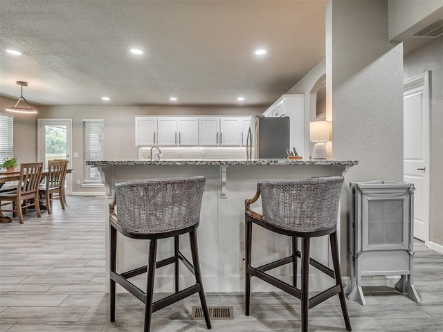 6513 NW 95th St, Oklahoma City, OK 73162 - kitchen with freestanding refrigerator, light stone counters, white cabinetry, a kitchen breakfast bar, and recessed lighting