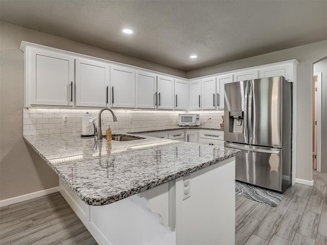 6513 NW 95th St, Oklahoma City, OK 73162 - kitchen featuring stainless steel fridge, a sink, white cabinets, decorative backsplash, and a peninsula