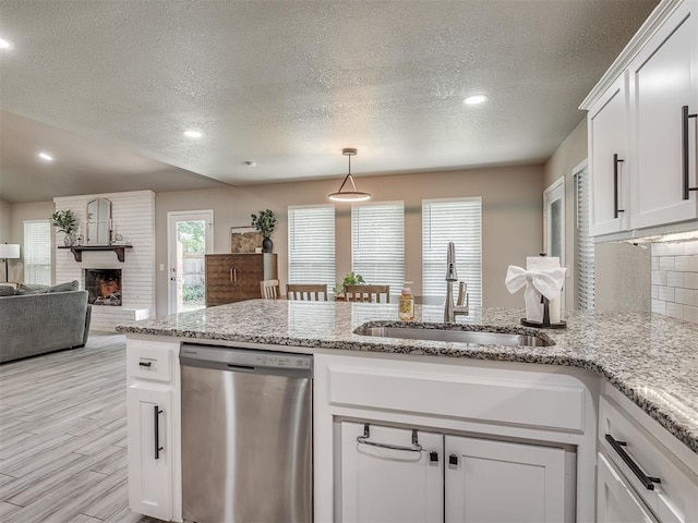 6513 NW 95th St, Oklahoma City, OK 73162 - kitchen featuring dishwasher, a sink, a textured ceiling, a brick fireplace, and white cabinets