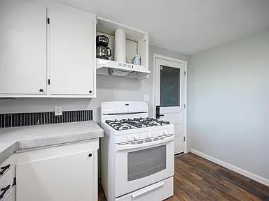 309 E Memorial St, Broken Bow, OK 74728 - kitchen with white range with gas cooktop, white cabinetry, under cabinet range hood, dark wood-type flooring, and light countertops