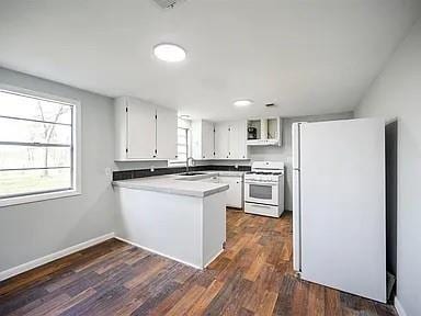 309 E Memorial St, Broken Bow, OK 74728 - kitchen with range, freestanding refrigerator, a peninsula, white cabinetry, and dark wood-style flooring