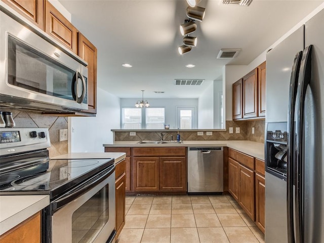 724 Ga Zump Dr, Norman, OK 73069 - kitchen featuring appliances with stainless steel finishes, a sink, a chandelier, backsplash, and brown cabinets