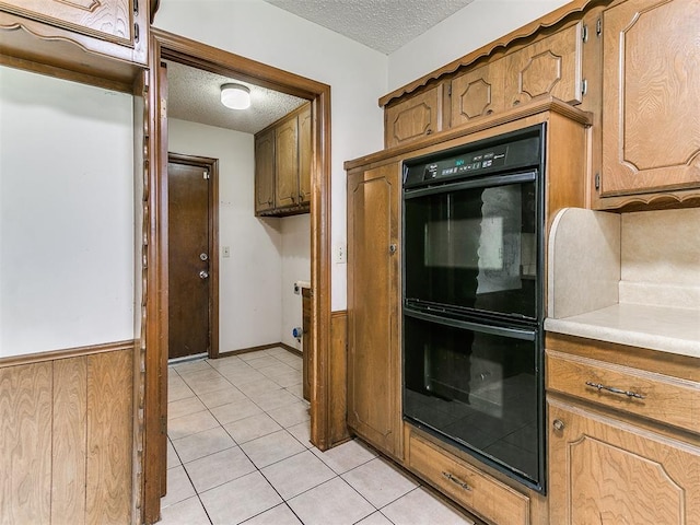 5201 SE 53rd St, Oklahoma City, OK 73135 - kitchen featuring a textured ceiling, light tile patterned floors, light countertops, brown cabinets, and a wainscoted wall