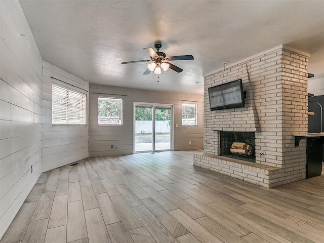 1117 Washington St, Edmond, OK 73034 - unfurnished living room with a ceiling fan, wood finished floors, a fireplace, plenty of natural light, and wood walls