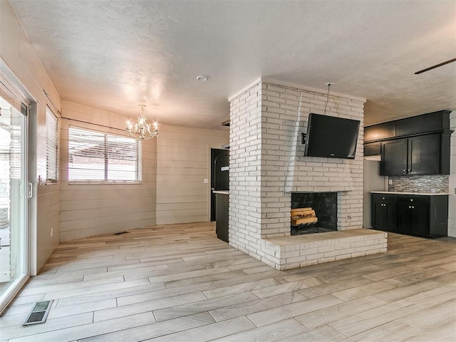 1117 Washington St, Edmond, OK 73034 - unfurnished living room featuring light wood-style flooring, a brick fireplace, a chandelier, and a textured ceiling
