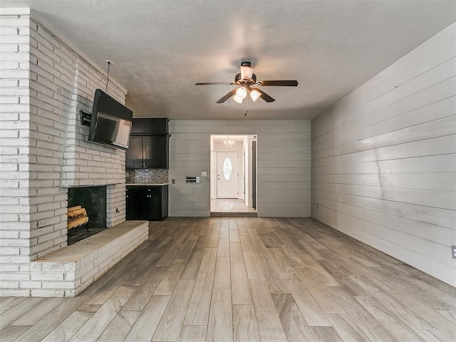 1117 Washington St, Edmond, OK 73034 - unfurnished living room with ceiling fan, light wood finished floors, a brick fireplace, and wood walls
