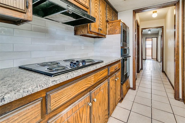 1405 Creston Way, Edmond, OK 73012 - kitchen featuring under cabinet range hood, black appliances, light tile patterned flooring, brown cabinetry, and tasteful backsplash